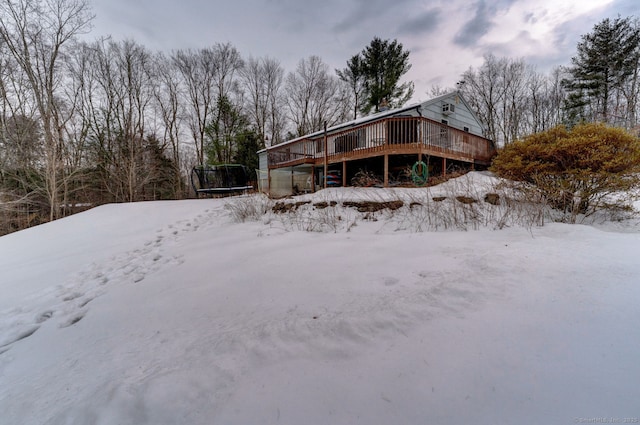 snow covered back of property with a deck and a trampoline