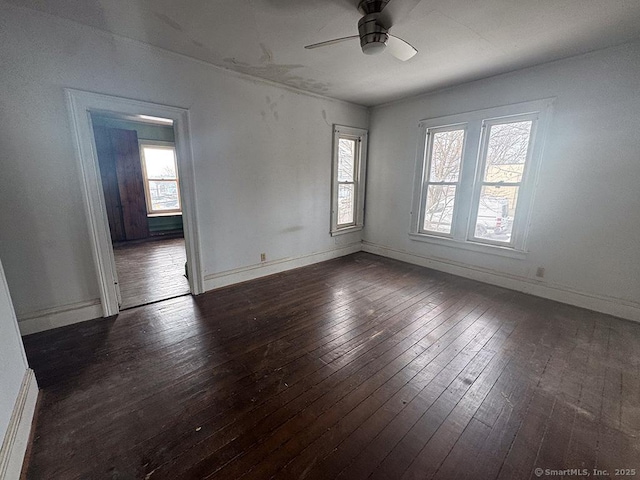 empty room featuring dark wood-type flooring, baseboards, and a ceiling fan