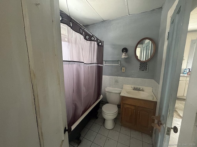 bathroom featuring tile patterned flooring, toilet, vanity, tile walls, and wainscoting