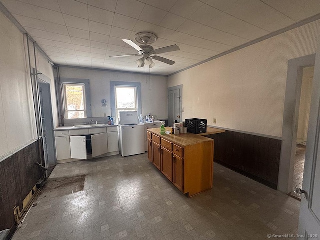 kitchen featuring washer / dryer, brown cabinetry, wood counters, a center island, and a sink