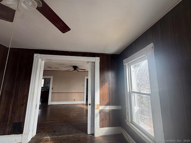 hallway featuring dark wood-type flooring, wooden walls, and baseboards