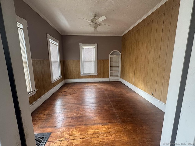 spare room with ornamental molding, a wainscoted wall, dark wood finished floors, and a textured ceiling