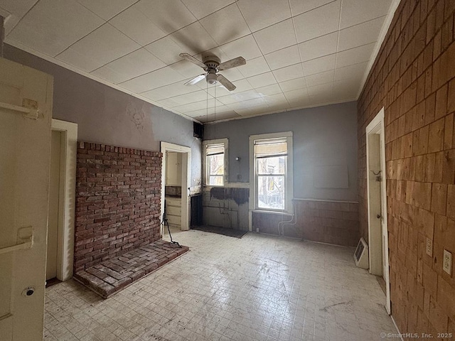 unfurnished living room with light floors, brick wall, ornamental molding, and a ceiling fan