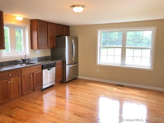 kitchen with dark countertops, light wood finished floors, baseboards, appliances with stainless steel finishes, and a sink