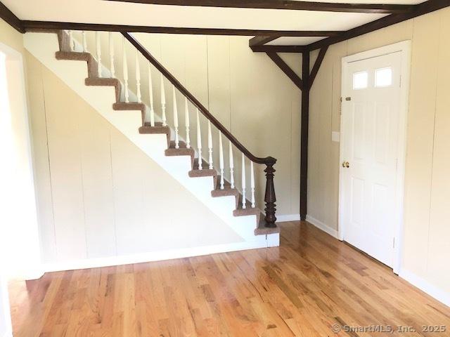 foyer entrance with beam ceiling, stairs, baseboards, and wood finished floors