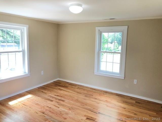 empty room featuring baseboards, light wood-style floors, and ornamental molding