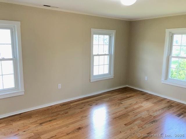 empty room with visible vents, wood finished floors, baseboards, and ornamental molding