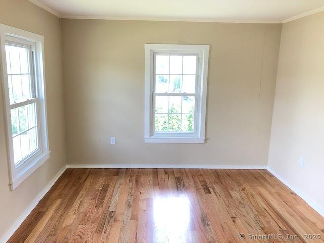 spare room featuring crown molding, wood finished floors, and baseboards