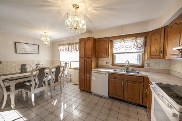 kitchen featuring white appliances, brown cabinetry, light countertops, pendant lighting, and a sink