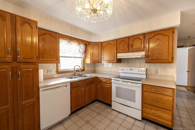 kitchen featuring under cabinet range hood, white appliances, a sink, light countertops, and brown cabinets