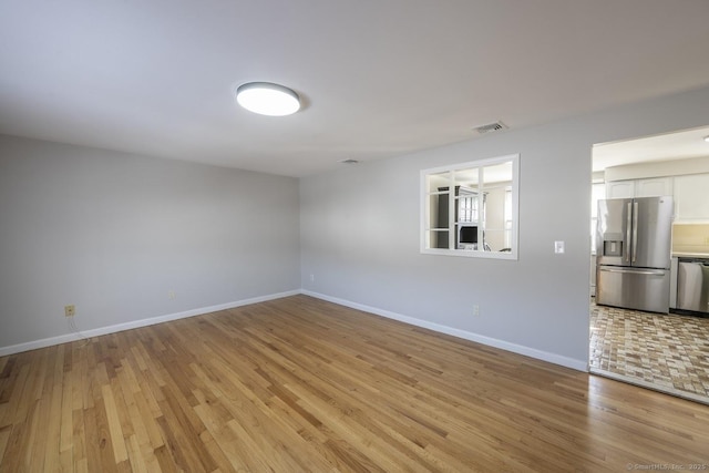 empty room with light wood-type flooring, visible vents, and baseboards