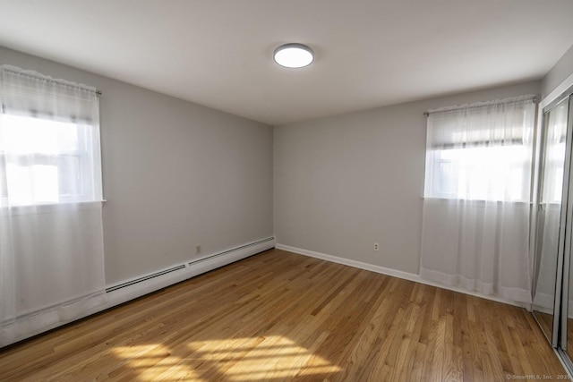 empty room with baseboards, light wood finished floors, baseboard heating, and a healthy amount of sunlight