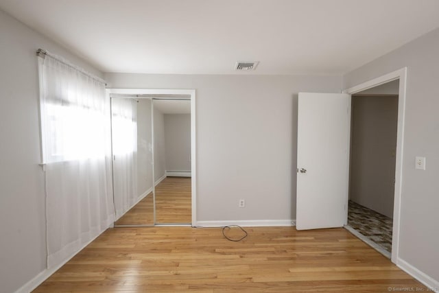 unfurnished bedroom featuring a baseboard heating unit, light wood finished floors, a closet, and visible vents