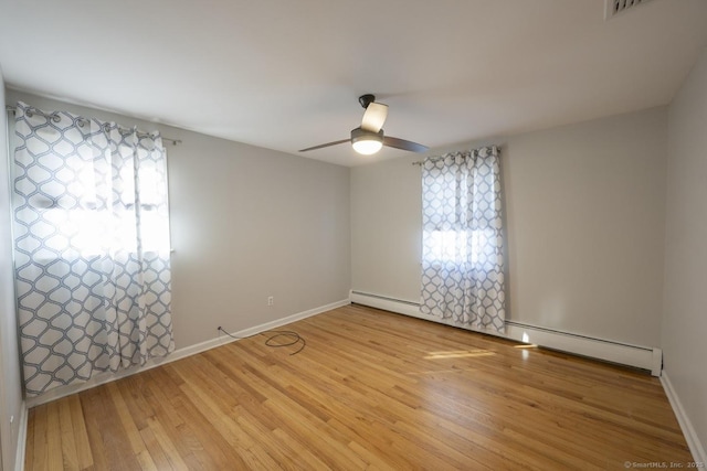 unfurnished room with light wood-style flooring, a baseboard heating unit, and a wealth of natural light