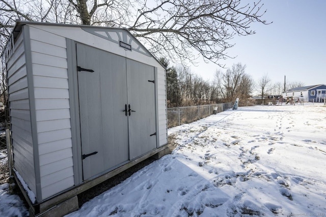 snow covered structure with a shed, an outdoor structure, and fence