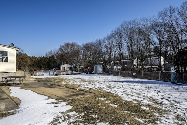 snowy yard featuring a storage shed and fence