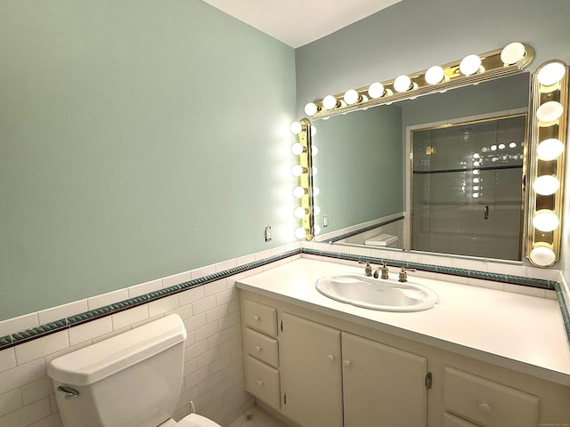 bathroom with toilet, a wainscoted wall, a shower with door, vanity, and tile walls