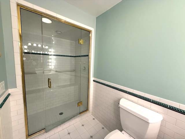 bathroom with tile patterned flooring, toilet, tile walls, wainscoting, and a shower stall