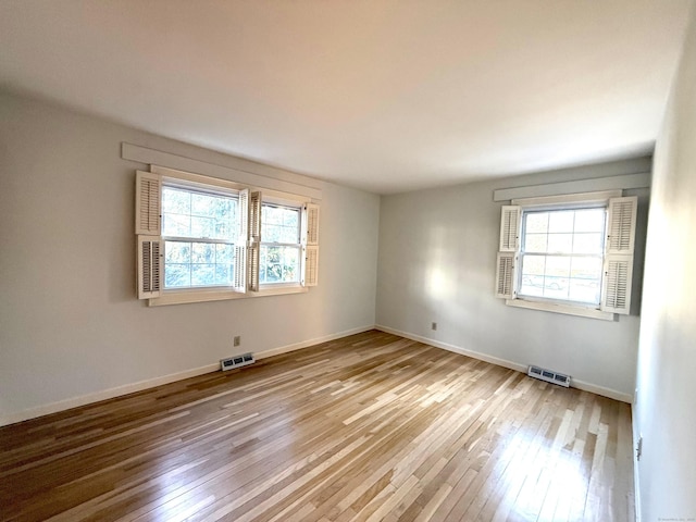 empty room with light wood-type flooring, visible vents, and baseboards