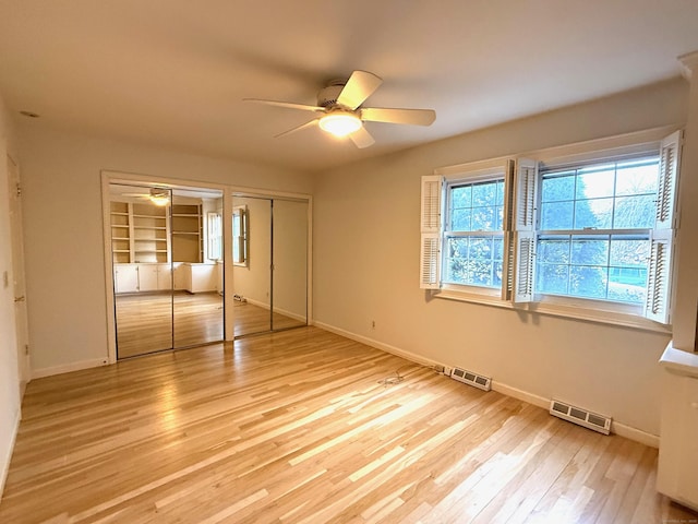 unfurnished bedroom with light wood-style flooring, two closets, visible vents, and baseboards