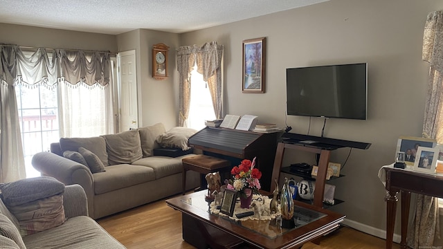 living room with a textured ceiling, light wood-type flooring, and baseboards