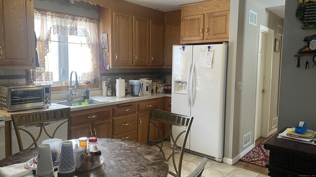 kitchen featuring white refrigerator with ice dispenser, visible vents, brown cabinets, and a sink