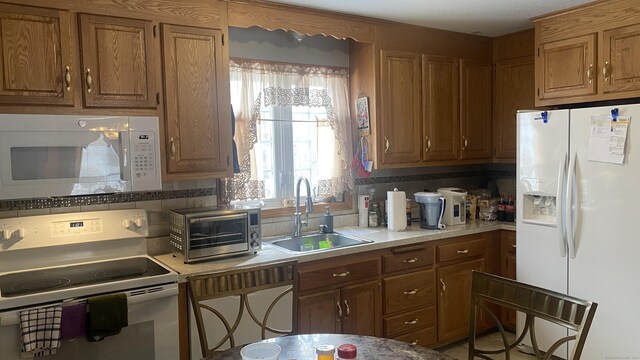 kitchen with a toaster, white appliances, a sink, light countertops, and brown cabinets