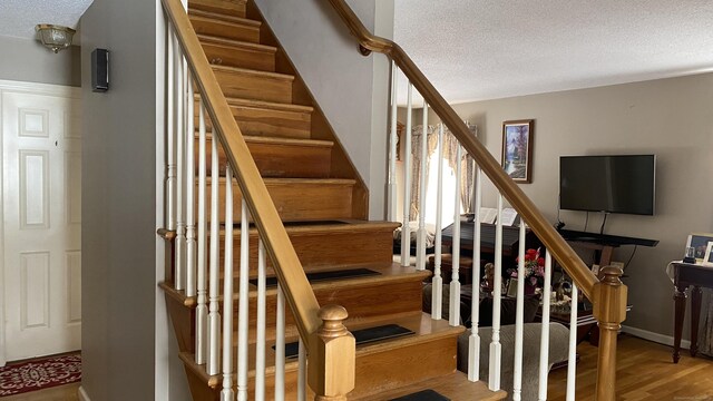 stairway with a textured ceiling, wood finished floors, and baseboards