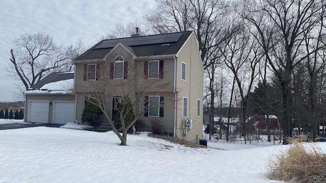 view of front of house with central AC unit, a chimney, an attached garage, and roof mounted solar panels