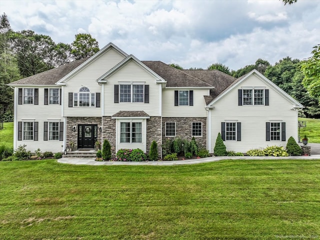 view of front of house featuring stone siding, a front lawn, and roof with shingles