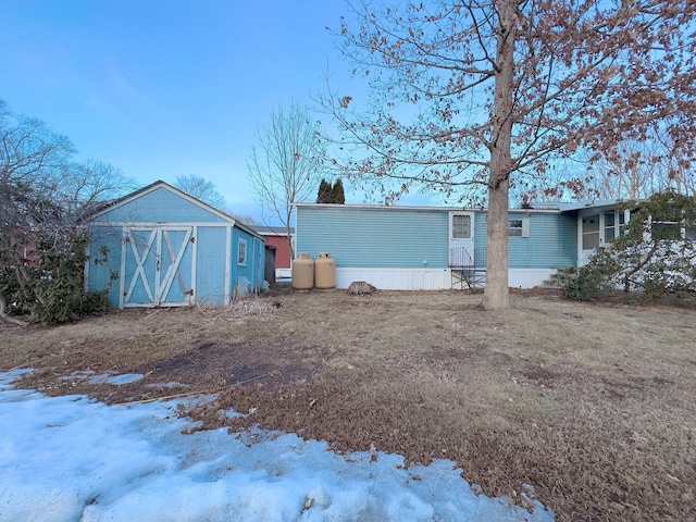 snow covered back of property with an outdoor structure and a storage shed