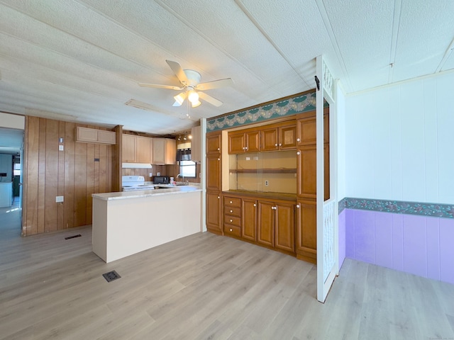 kitchen with a peninsula, a textured ceiling, light wood-style floors, brown cabinetry, and electric stove