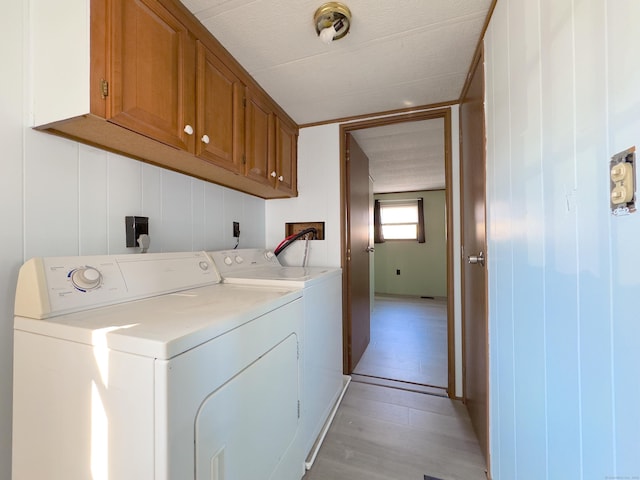 clothes washing area with light wood-type flooring, washing machine and clothes dryer, and cabinet space