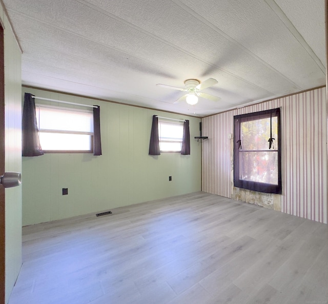 empty room with light wood-type flooring, a ceiling fan, visible vents, and a textured ceiling