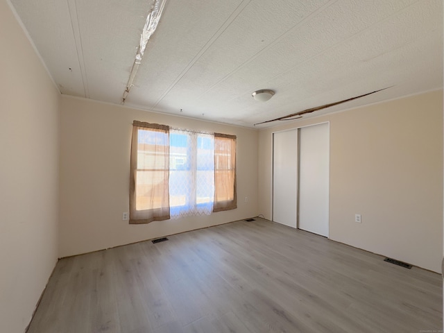 unfurnished bedroom with a closet, visible vents, light wood-style flooring, and a textured ceiling