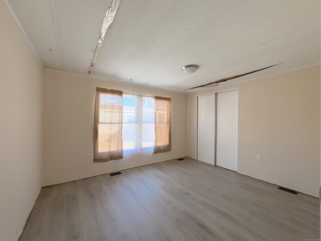 empty room with visible vents, light wood finished floors, and a textured ceiling