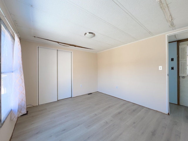 unfurnished bedroom featuring a textured ceiling, visible vents, a closet, and light wood-style flooring