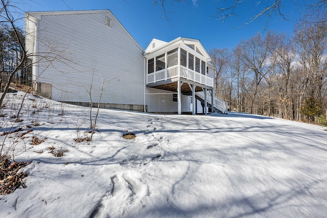 snow covered rear of property featuring a sunroom, stairway, and a carport