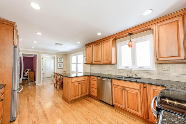 kitchen with appliances with stainless steel finishes, a peninsula, a sink, light wood-type flooring, and backsplash