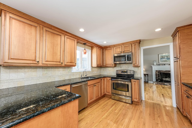 kitchen featuring light wood-style flooring, decorative backsplash, appliances with stainless steel finishes, a sink, and dark stone countertops