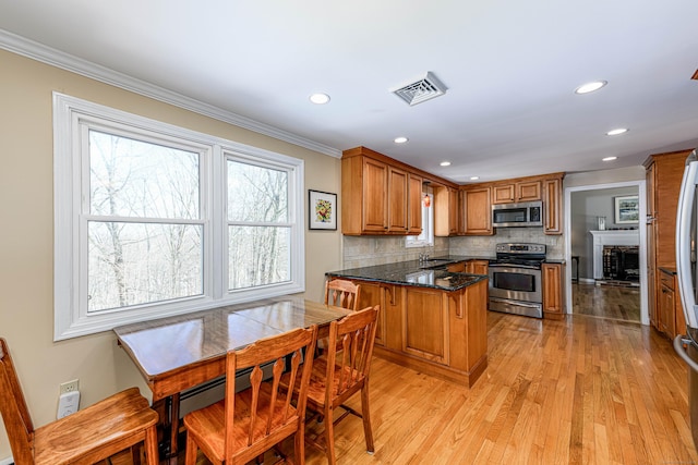 kitchen with brown cabinets, stainless steel appliances, visible vents, a sink, and a peninsula