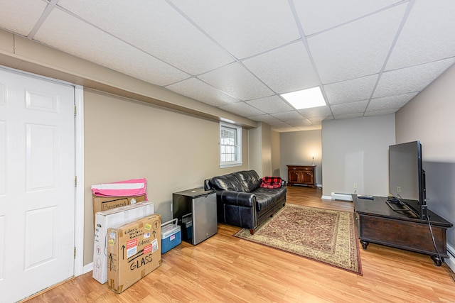 living room featuring light wood-type flooring, a baseboard heating unit, baseboards, and a drop ceiling