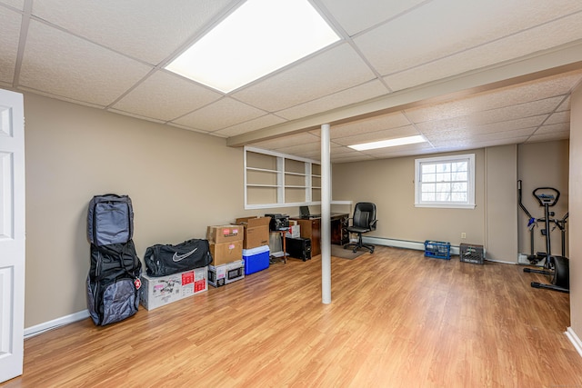 exercise room with a baseboard radiator, a drop ceiling, baseboards, and wood finished floors