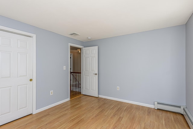 unfurnished bedroom with a baseboard heating unit, light wood-type flooring, visible vents, and baseboards