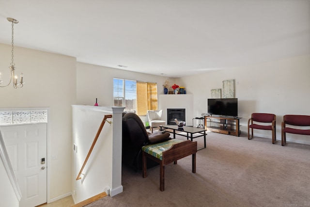 living area featuring a glass covered fireplace, baseboards, light carpet, and a chandelier