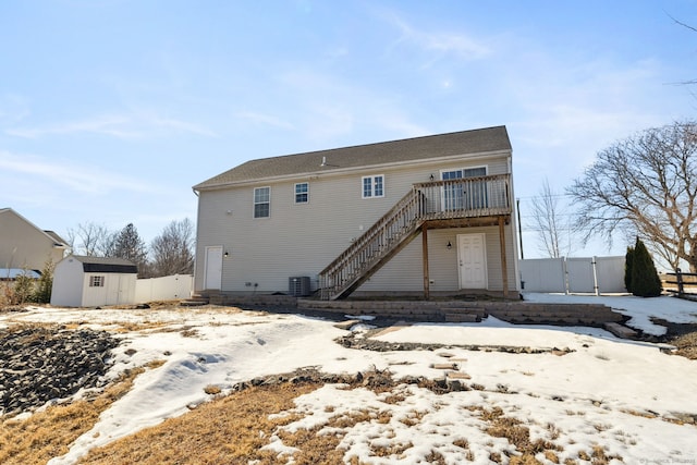 snow covered back of property featuring central AC, a storage shed, an outdoor structure, and fence