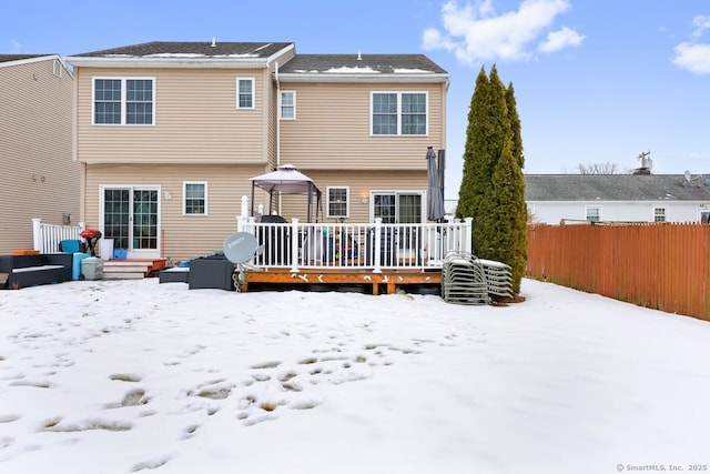 snow covered rear of property with entry steps, fence, and a wooden deck