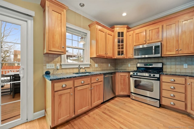 kitchen featuring a sink, appliances with stainless steel finishes, light wood finished floors, glass insert cabinets, and pendant lighting