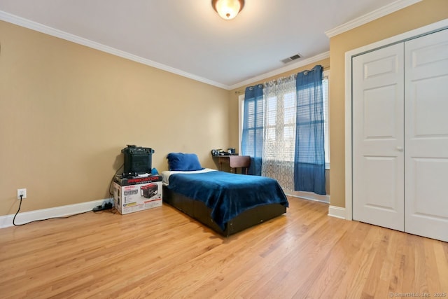 bedroom featuring wood finished floors, visible vents, baseboards, a closet, and crown molding