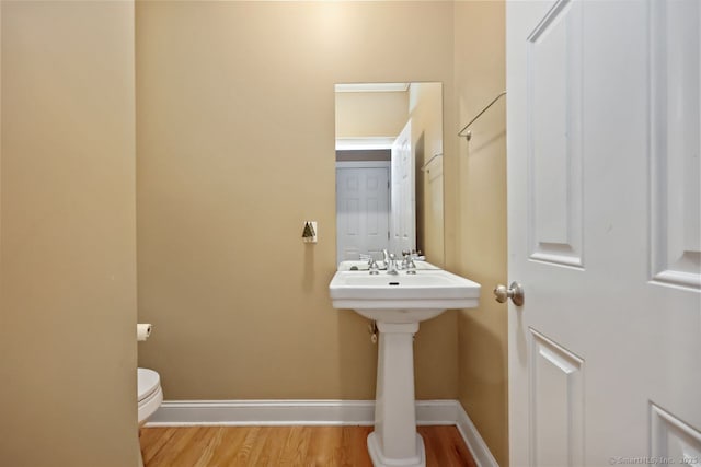 half bathroom featuring toilet, a sink, baseboards, and wood finished floors